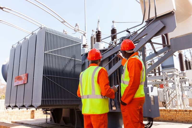 Workers inspecting a power transformer in a substation