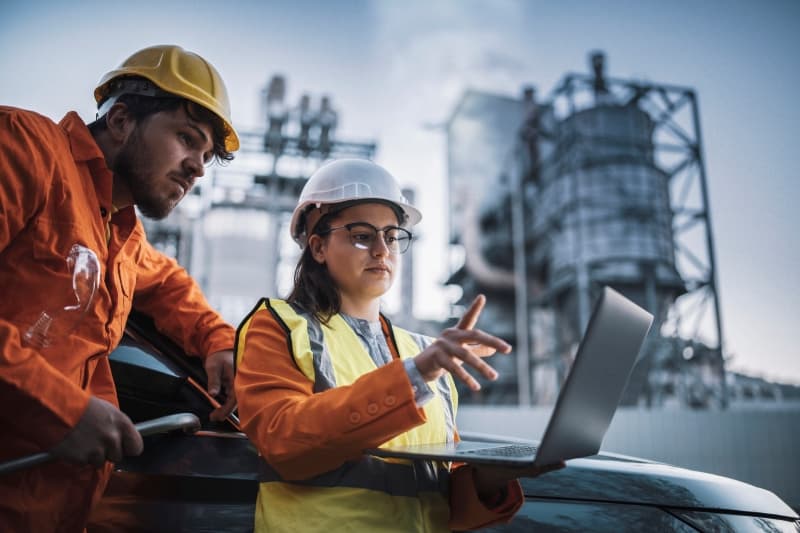 Engineers wearing helmets checking a tablet at a power plant
